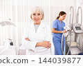 Smiling old woman doctor posing against background of cosmetology devices 144039877