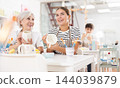Cheerful elderly and young wowen painting mugs in pottery masterclass 144039879